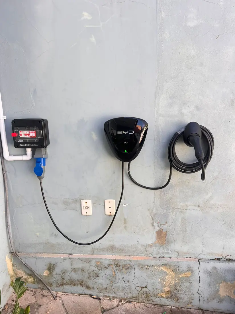 Carregador BYD com cabo enrolado em parede externa, ao lado do quadro de proteção Clamper Mobi Box